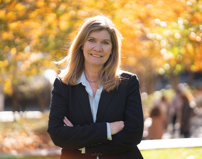 Sarah Banet-Weiser standing outside on a fall day smiling at the camera with her arms crossed